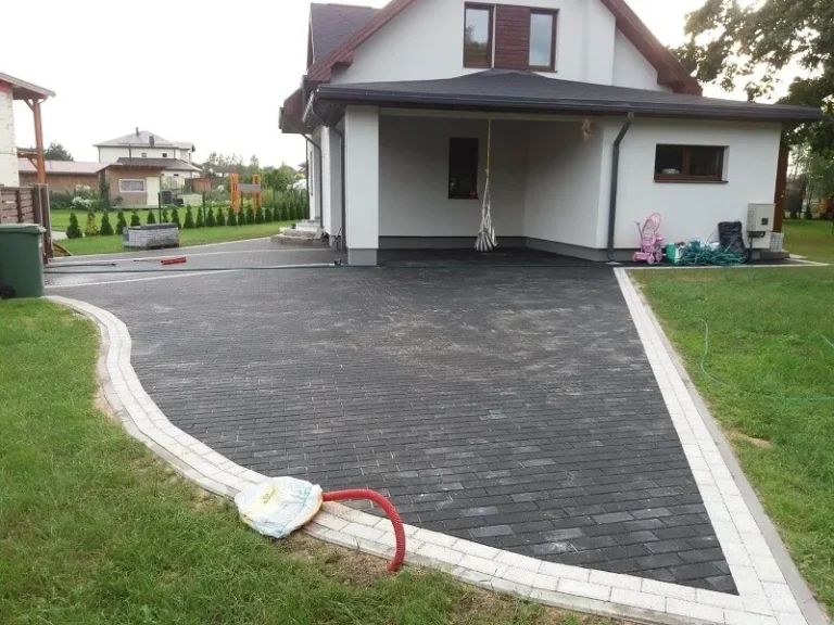 Tumšs bruģakmens pie privātmājas ar gaišu apmali gar izliektu malu