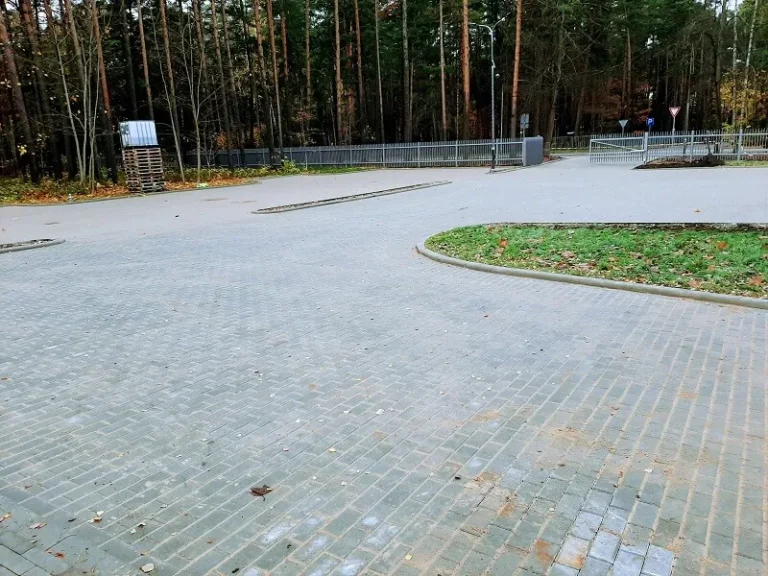 Komercobjekta stāvvieta no bruģakmens ar apmalēm un zaļo saliņu